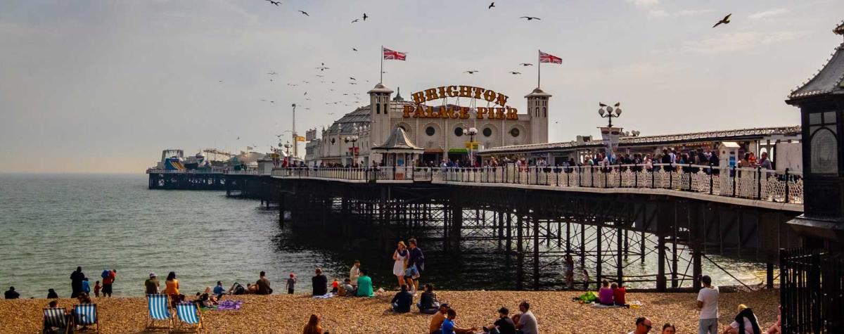 People on a Pebble Beach next to the Brighton Pier which Extends out to Sea